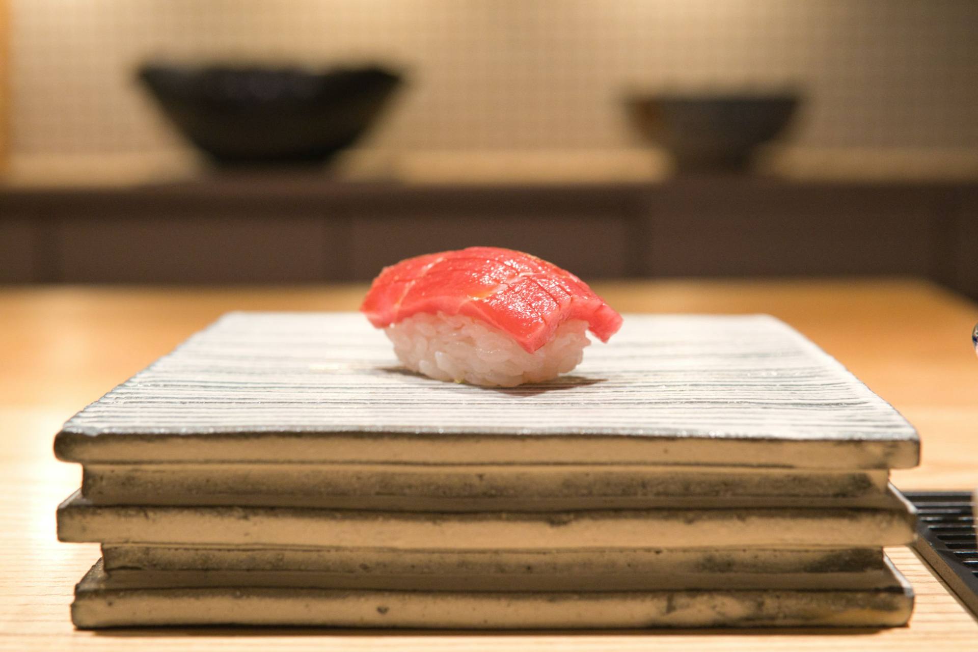 A single piece of nigiri, hand-shaped and set on a stone plate